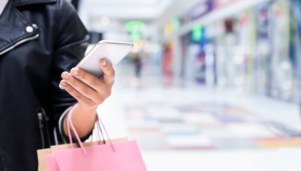 Woman shopping in mall holding smartphone and pink shopping bag