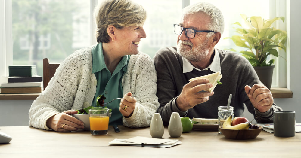Elderly couple sitting at kitchen table eating breakfast