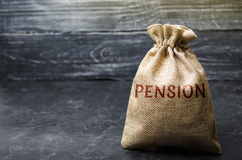 bag full of coins marked pension on wooden background