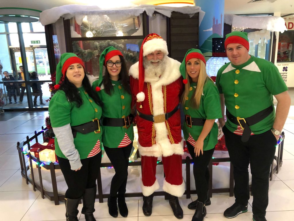 Members of staff dressed as elves with Santa in front of his grotto